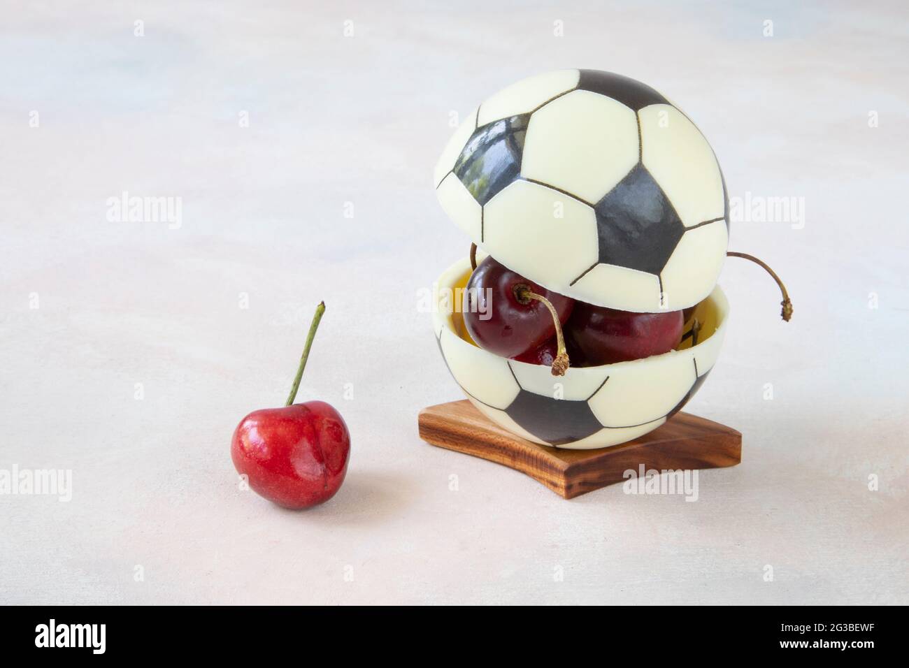 Chocolate ball for European football with cherry berries inside. Modern dessert concept for healthy watching of football matches with a delicious snac Stock Photo