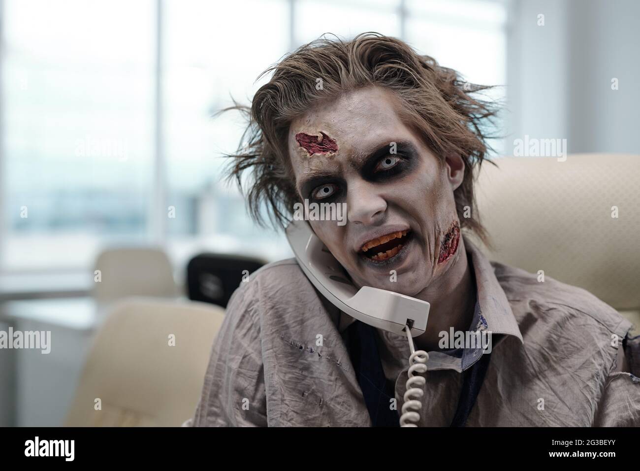 Ugly zombie businessman speaking on the phone by workplace in office Stock Photo