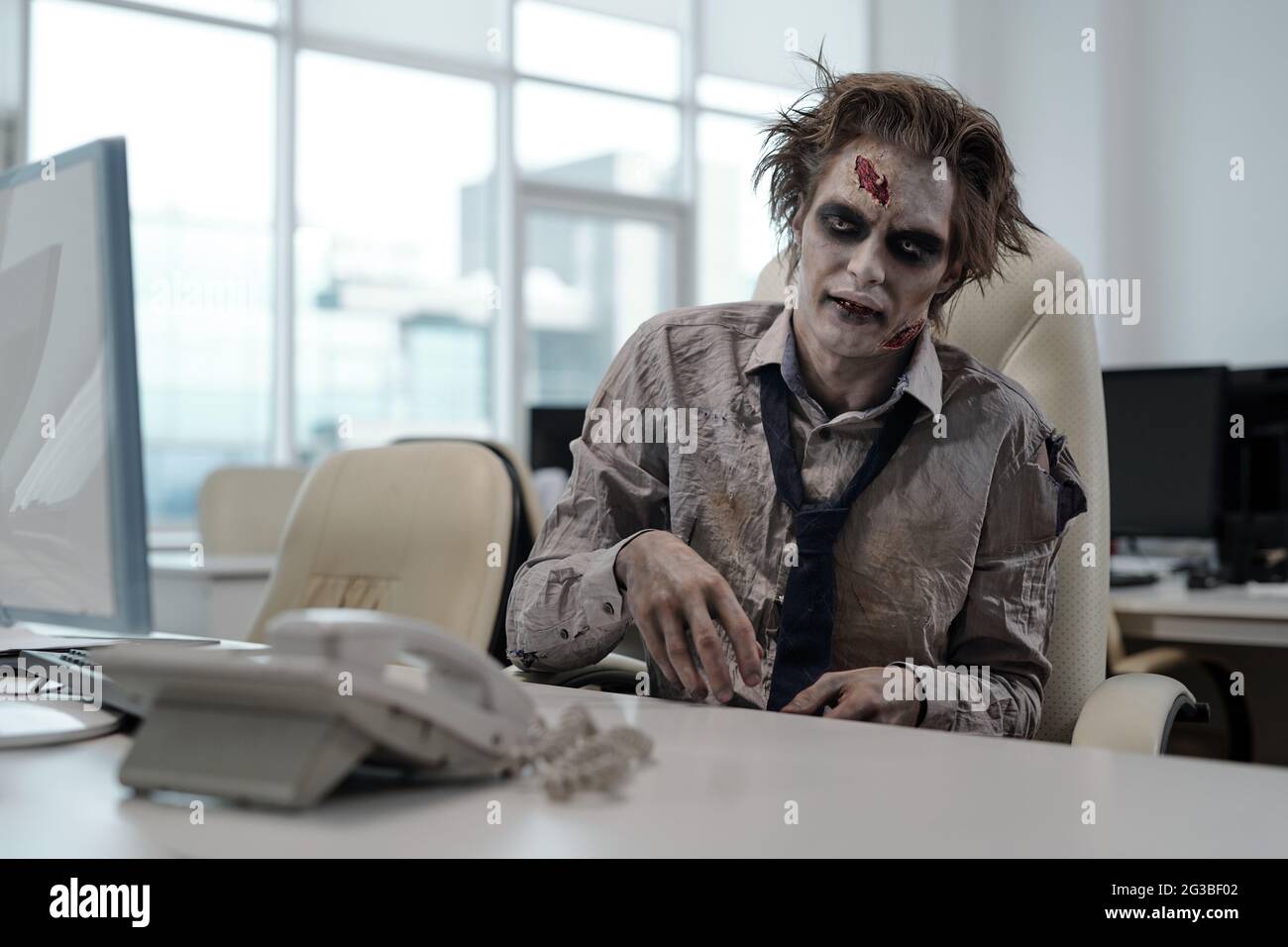 Zombie businessman sitting by desk in open space office Stock