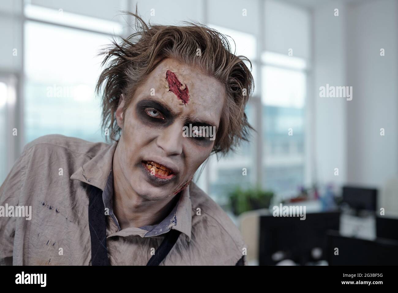 Young gloomy man with zombie stage makeup looking at camera in office Stock Photo