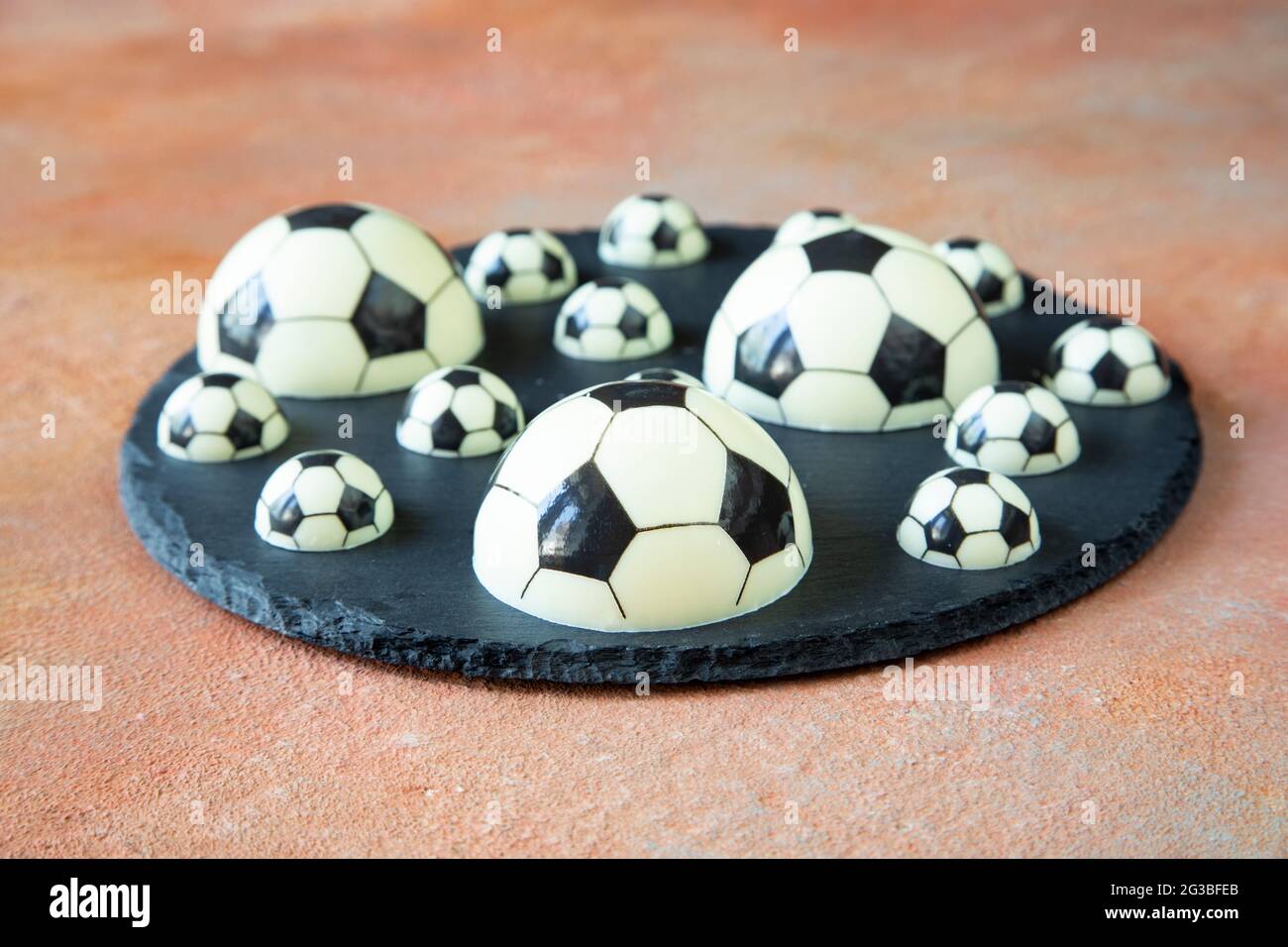 A delicious dessert of chocolate football balls of different shapes on a black serving plate - a concept of sports photography for a football fan Stock Photo
