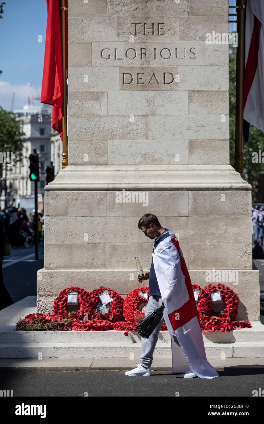 Patriotic England football fan draped in the St. George's Cross flag stood at the Cenotaph war memorial in Whitehall London, England, Stock Photo