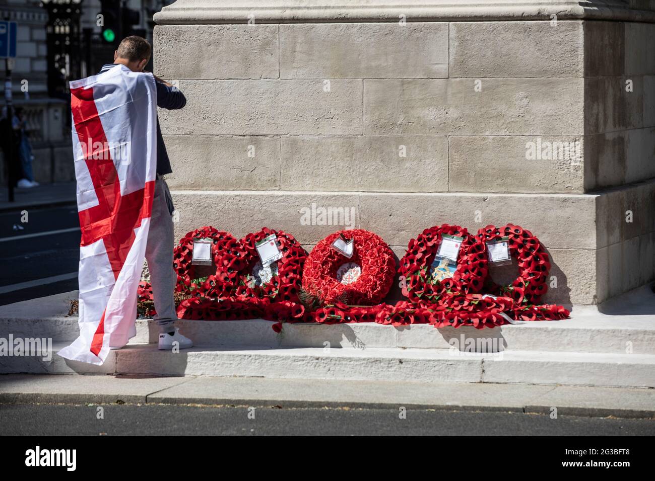 Patriotic England football fan draped in the St. George's Cross flag stood at the Cenotaph war memorial in Whitehall London, England, Stock Photo