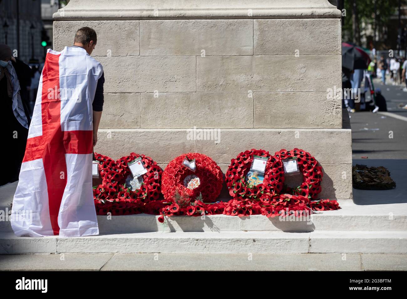 Patriotic England football fan draped in the St. George's Cross flag stood at the Cenotaph war memorial in Whitehall London, England, Stock Photo