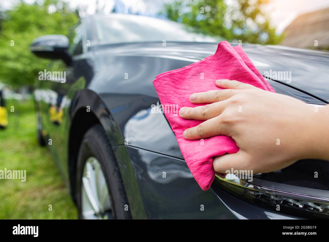A hand with a red rag wipes water drops on a car after washing with car
