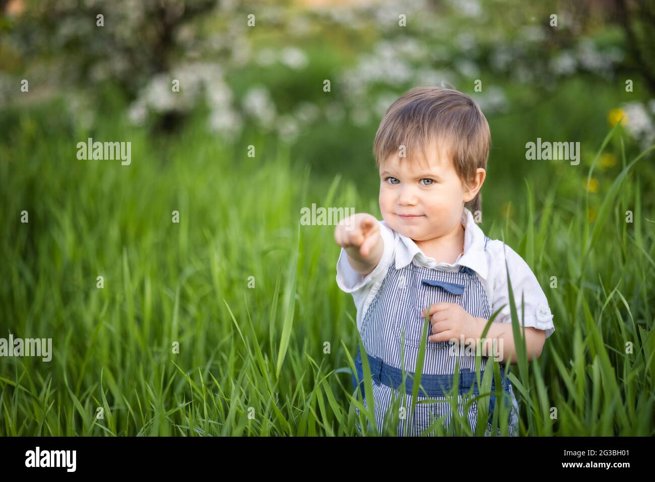 A little boy in denim overalls with expressive blue eyes. Jumping and  fooling around in the tall green grass against the backdrop of a large  green bus Stock Photo - Alamy