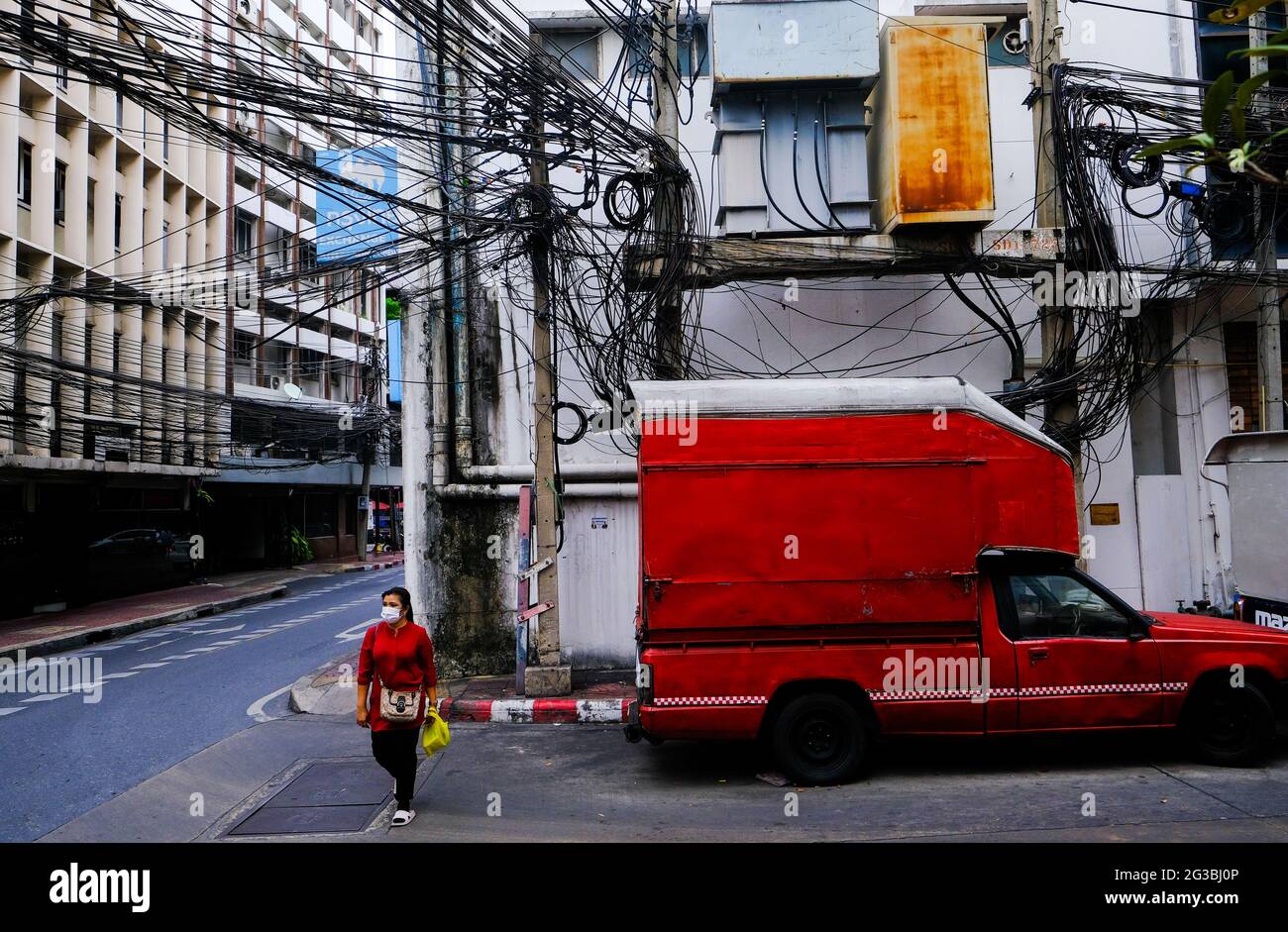 A woman walks past an old parked red van in an empty street in Chinatown, Bangkok, Thailand. Stock Photo