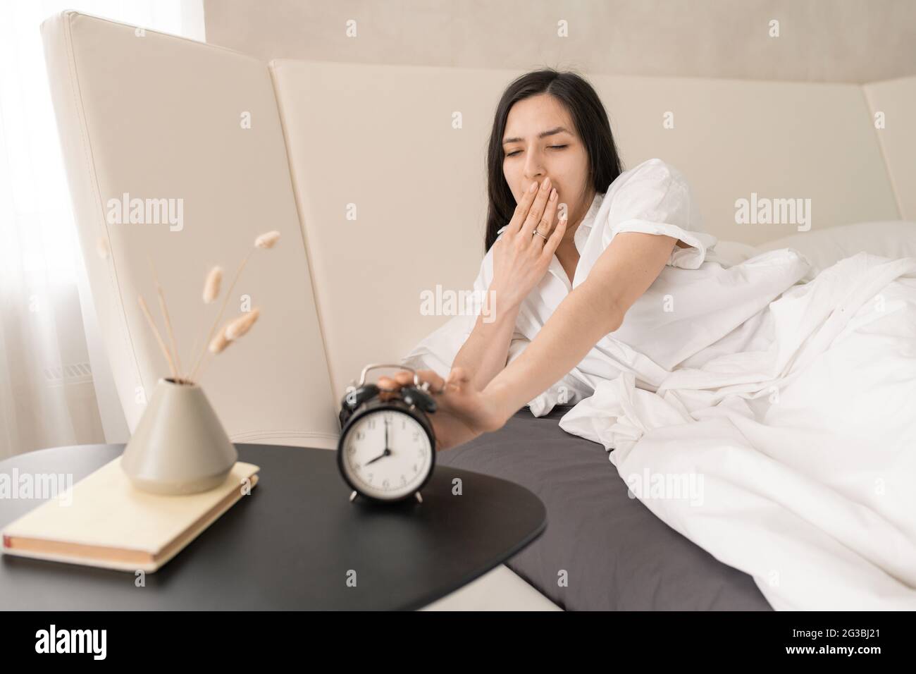 Girl stopping alarm clock and yawning after sleep Stock Photo Alamy