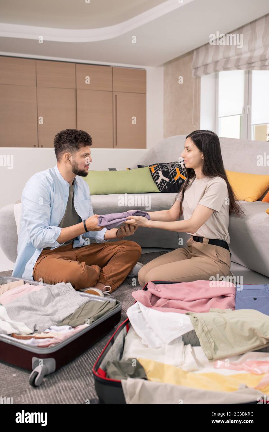 Happy couple packing clothes into suitcases while going for journey