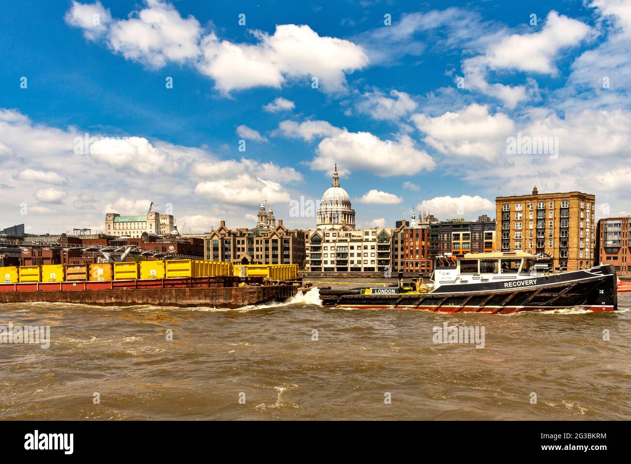 LONDON ENGLAND RIVER THAMES LONDON RECOVERY BOAT TOWING BARGE AND CONTAINERS ST. PAULS CATHEDRAL DOME IN THE BACKGROUND Stock Photo
