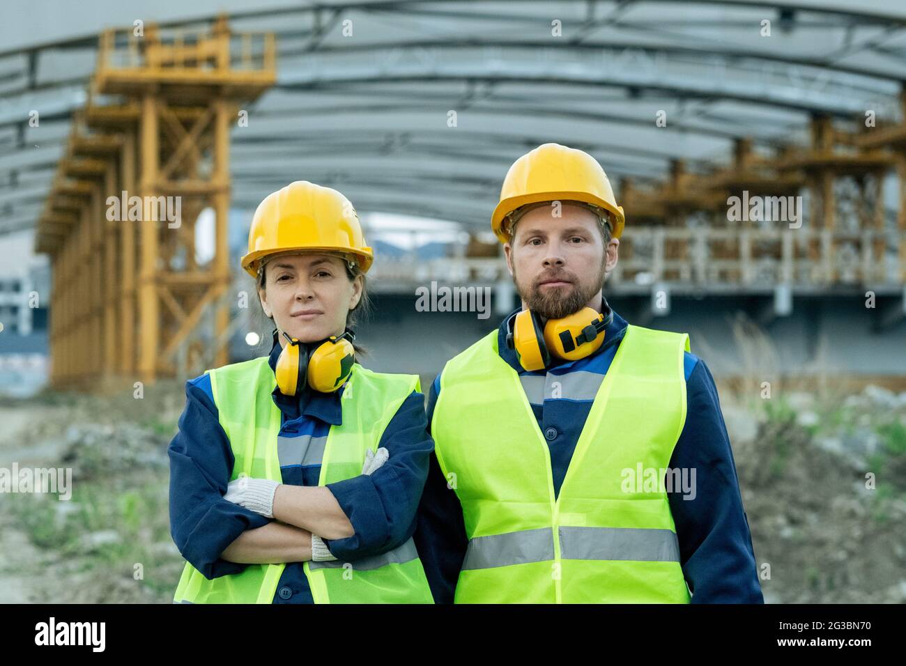 Two serious construction workers in uniform and helmets standing next ...