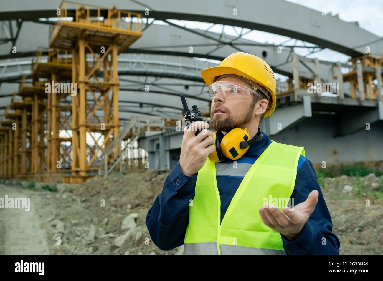 Young builder explaining something while speaking on walkie-talkie on construction site Stock Photo