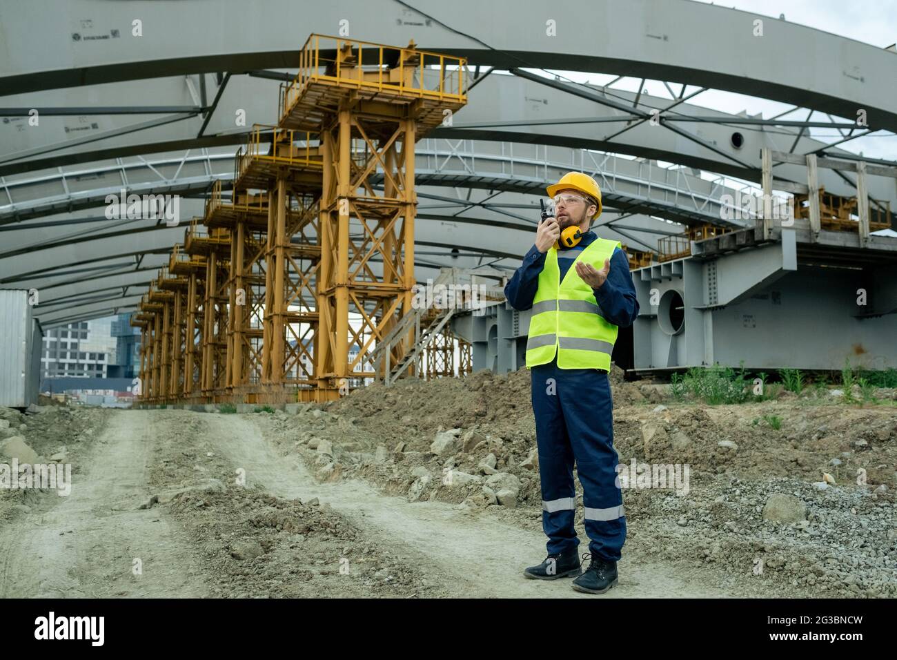 Contemporary builder using walkie-talkie against huge construction frame Stock Photo