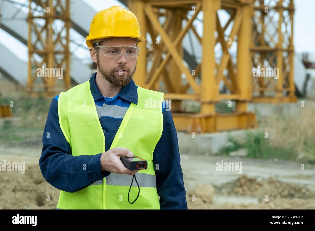 Young builder in uniform and protective helmet and eyeglasses using work tool Stock Photo