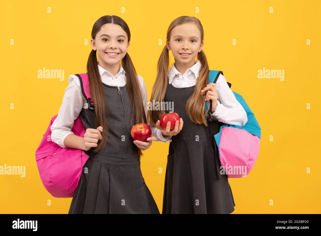Hungry kids in formal uniforms hold vitamin apples for school snack yellow background, snacking Stock Photo