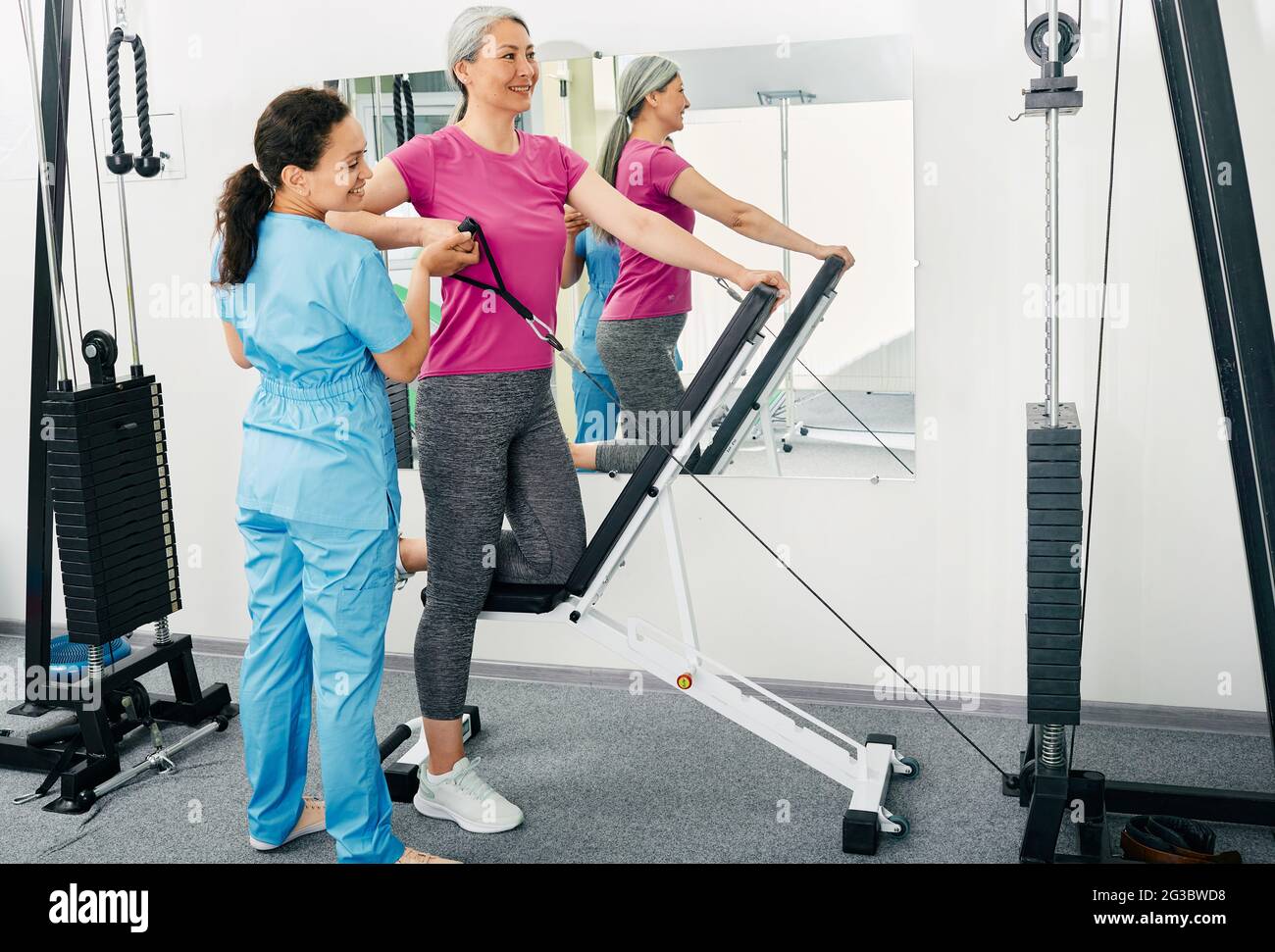 Mature woman patient at physiotherapy doing rehab exercises with her chiropractor using exercise machine Stock Photo