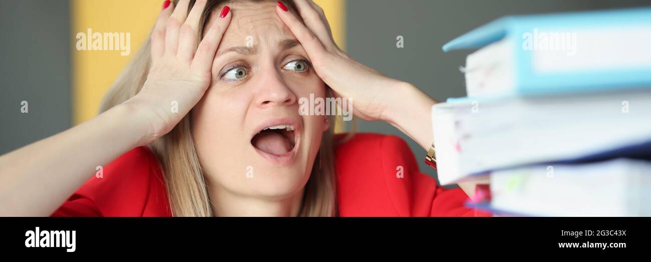Woman holding her head and is surprised in front of many folders on table Stock Photo