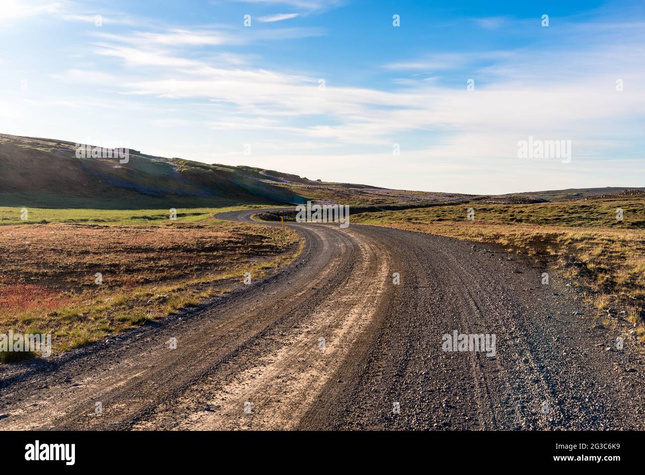 Empty winding gravel road in a barren landscape on a sunny summer day. Lens flare. Stock Photo