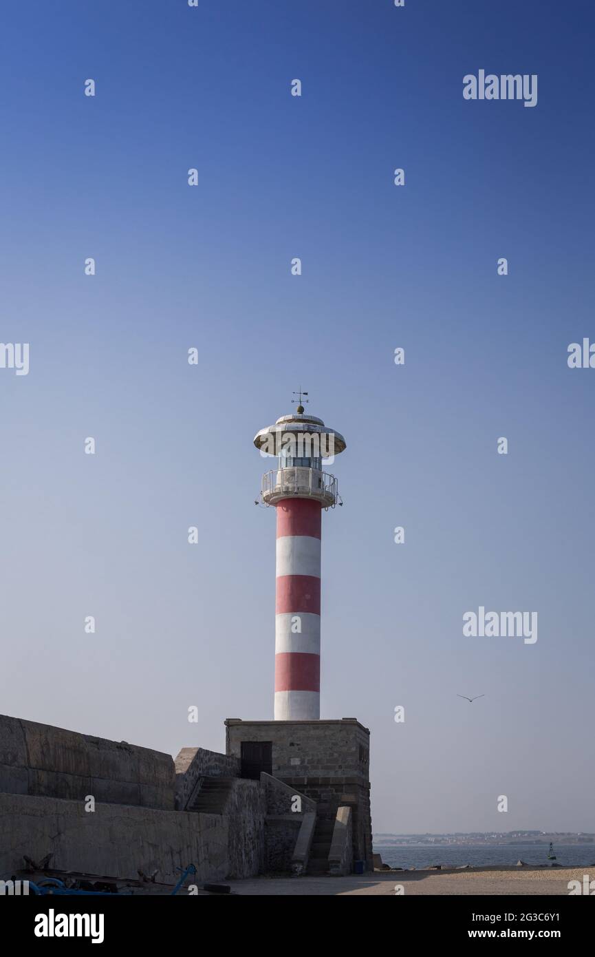 A view of the harbor with a large old red white lighthouse, pier against the blue sky and sea Stock Photo