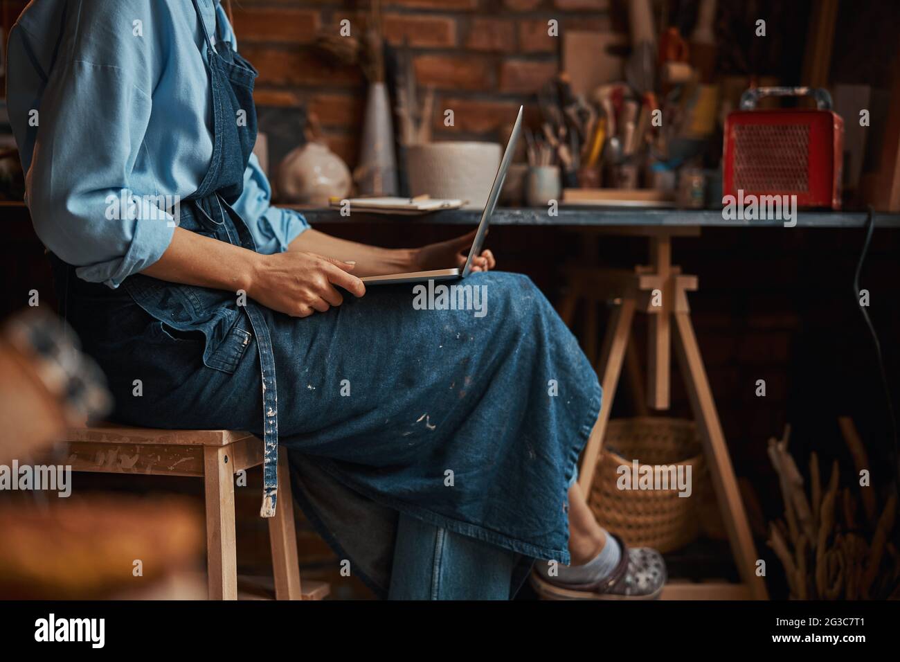 Beautiful elegant young sculptor spending time in pottery workshop while using internet in pottery workshop Stock Photo