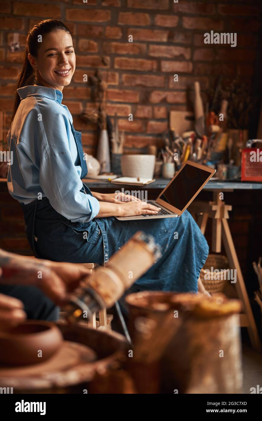 Young Caucasian female sculptor working in art studio while using internet Stock Photo
