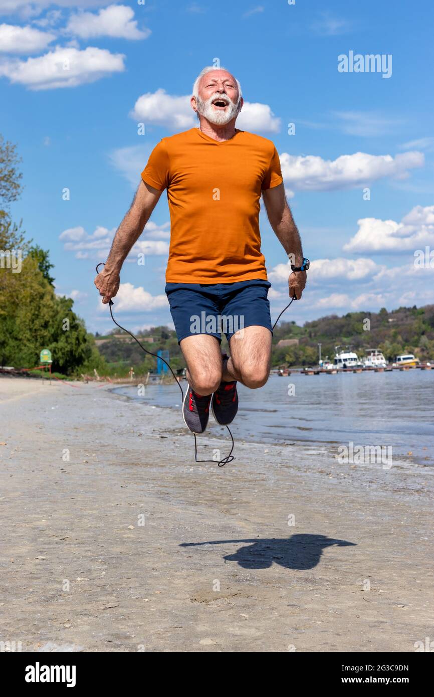 Active senior elderly man jumping the rope, exercising on the beach by