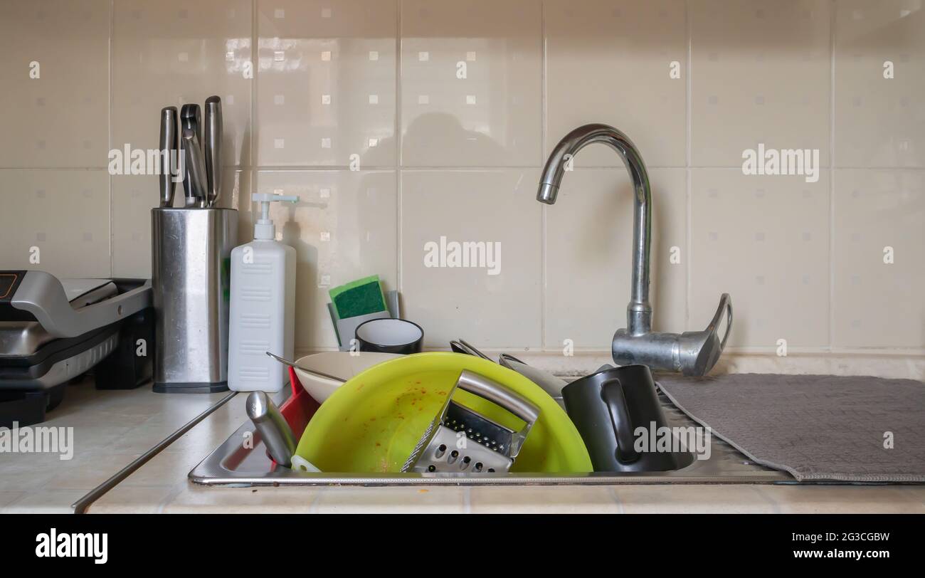 The kitchen utensils in the wash basin need to be washed. A pile of dirty dishes in the kitchen