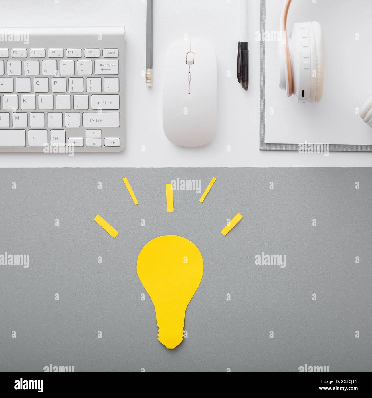 Yellow light bulb idea insight concept on student desktop with keyboard pc computer mouse headphones and white suppliers in workspace on gray table Stock Photo