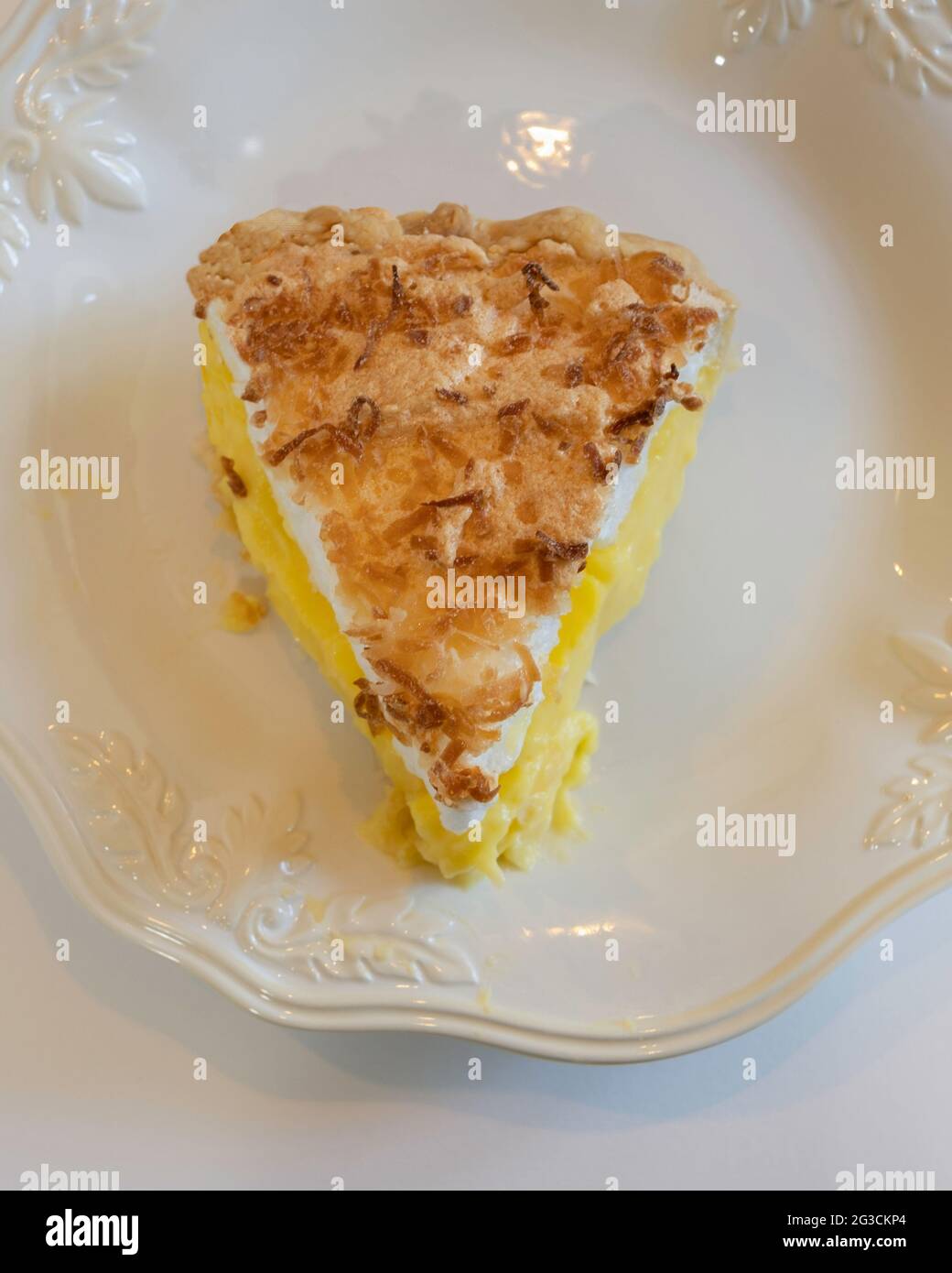 Slice of homemade coconut meringue cream pie on a white plate. White background. Stock Photo