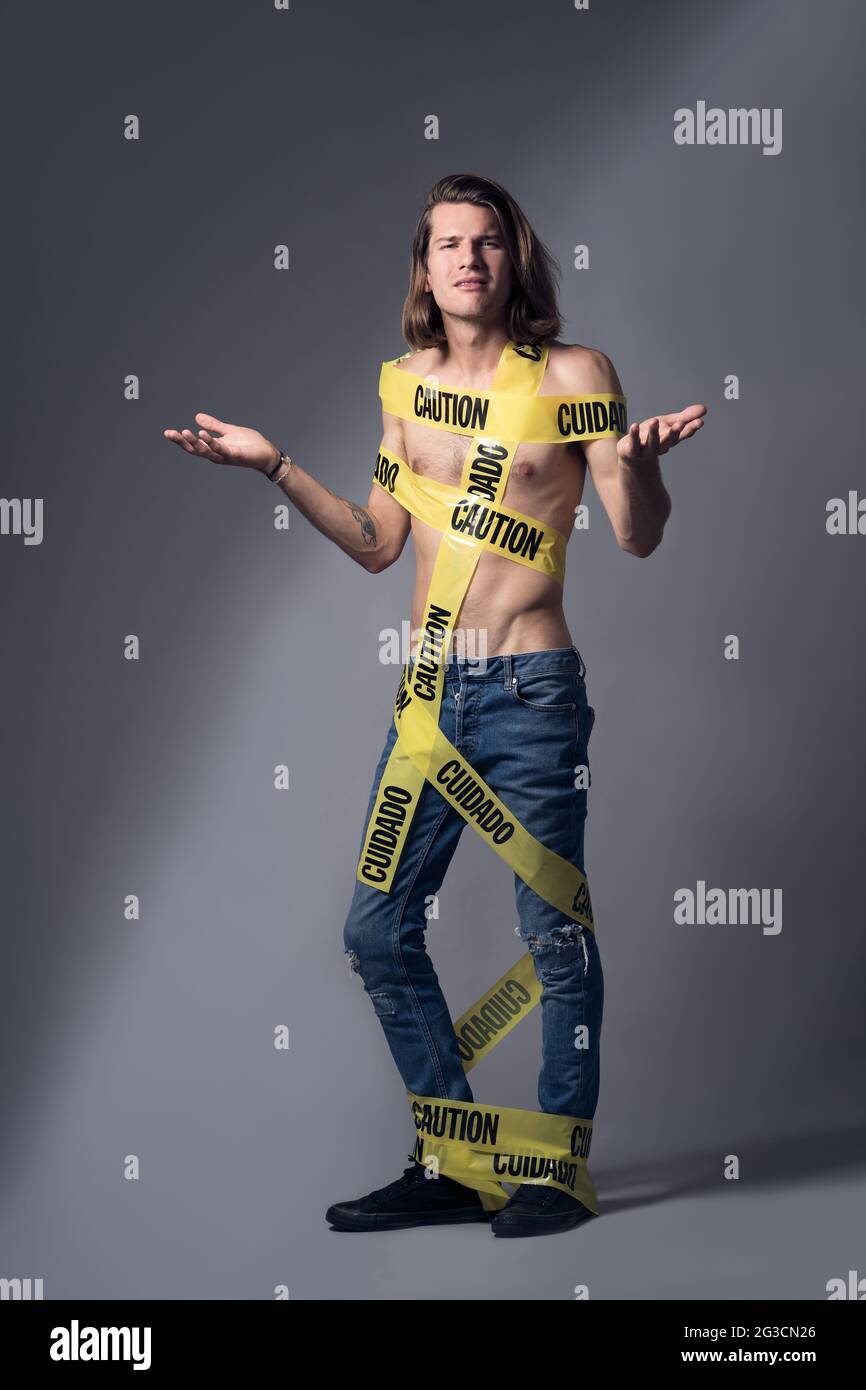 A white Caucasian male model, posing topless in jeans with a yellow caution tape wrapped around his body. A bad boy concept. Stock Photo