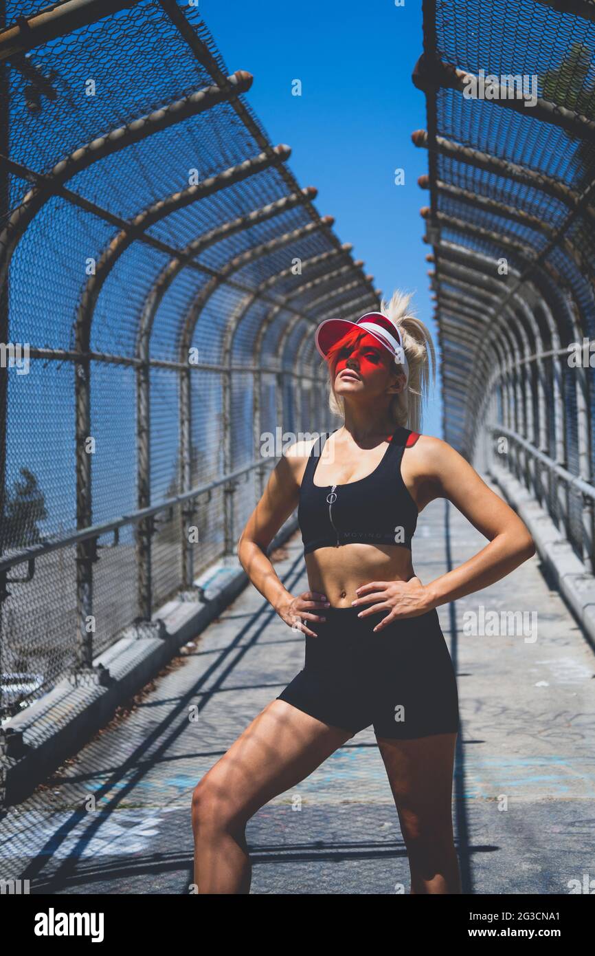 https://c8.alamy.com/comp/2G3CNA1/a-blonde-female-model-in-pony-tail-wearing-a-transparent-red-visor-hat-sports-bra-and-shorts-posing-with-her-two-hands-on-her-hip-2G3CNA1.jpg