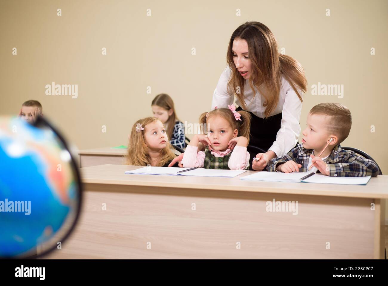 Primary school teacher helping a girl writing at her desk Stock Photo ...