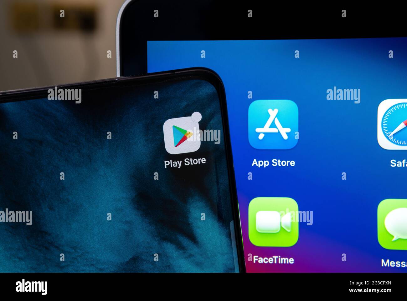 Google Play Store and blurred App Store apps seen on android smartphone and Apple macbook M1 laptop screens. Concept. Stafford, UK, June 15, 2021. Stock Photo