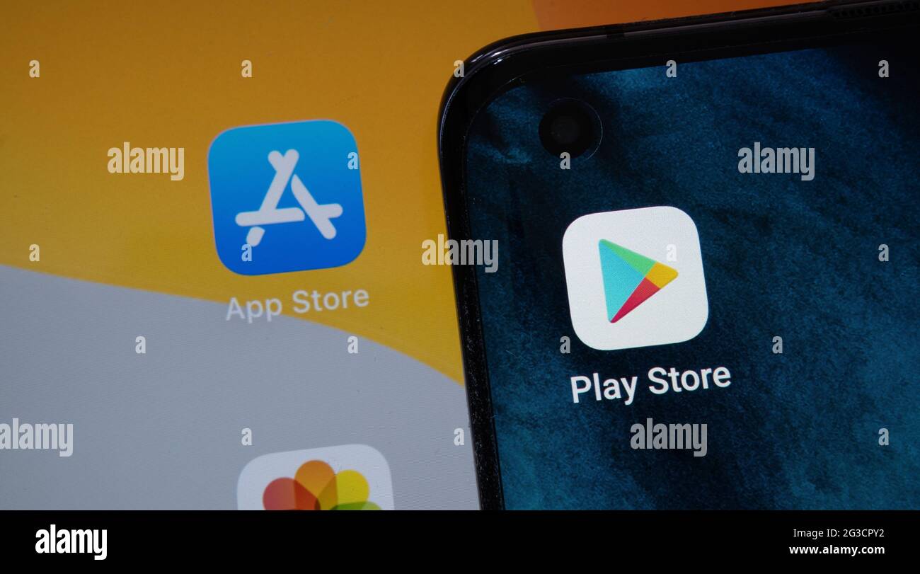 Google Play Store and blurred App Store apps seen on android smartphone and Apple macbook M1 laptop screens. Concept. Stafford, UK, June 15, 2021. Stock Photo