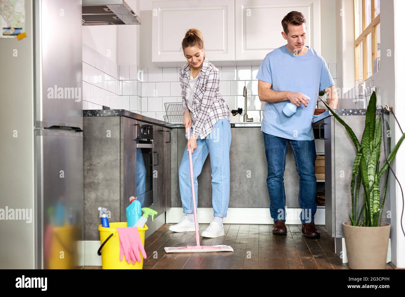 Two Janitors Cleaning Kitchen And Mopping Floor At Home, Caucasian Man And Woman In Casual Weae Enjoy Housekeeping, Cleaning Flat Apartment Stock Photo
