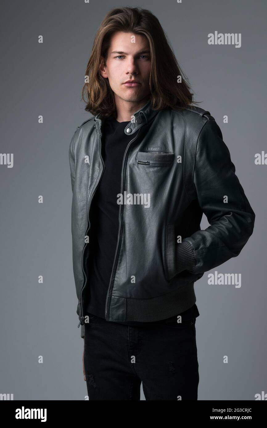 A portrait of a long hair caucasian male model wearing an 80s vintage gray leather jacket posing. Stock Photo