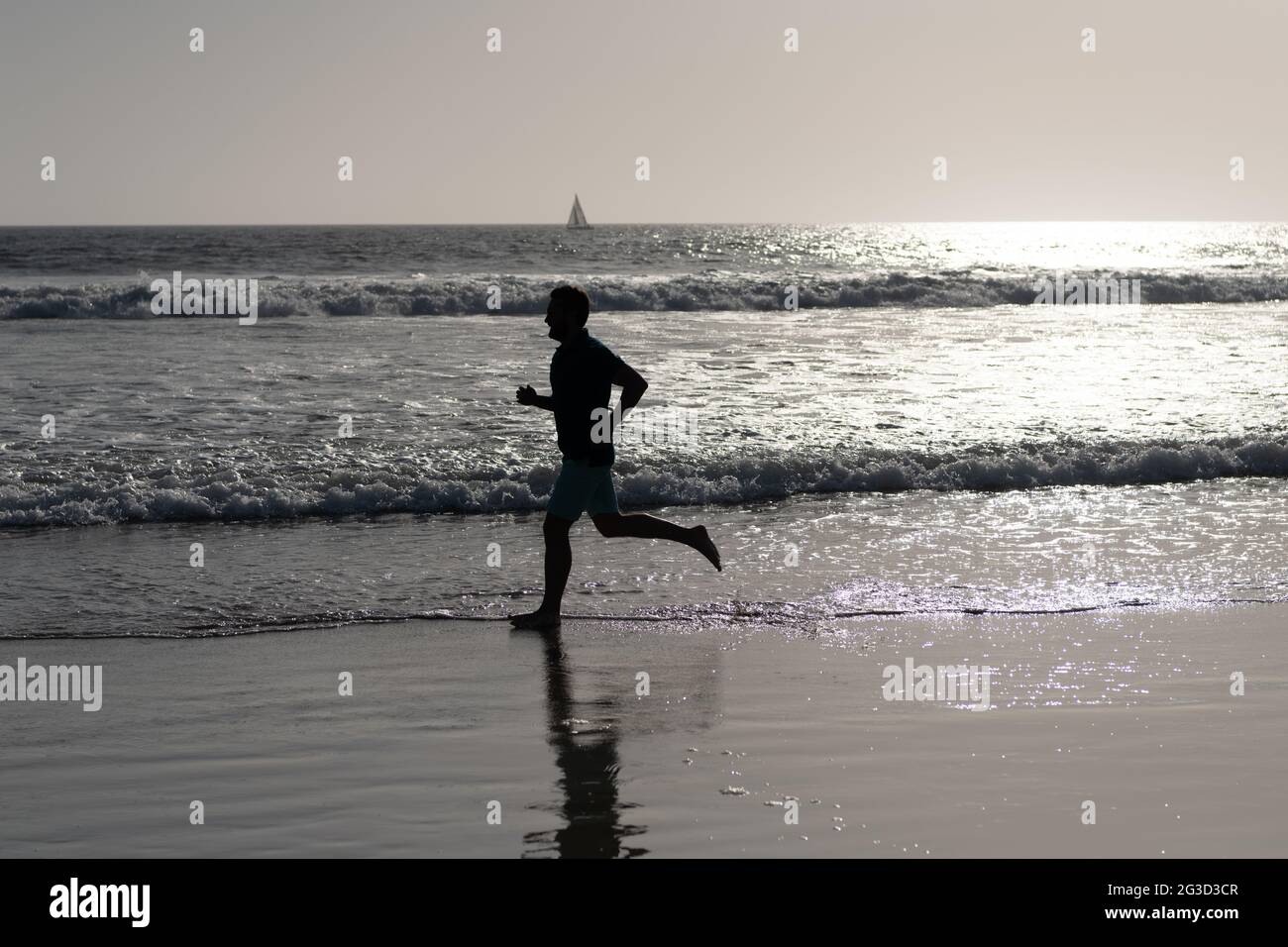 athletic man runner silhouette run on summer beach with sea water and sun, sport Stock Photo
