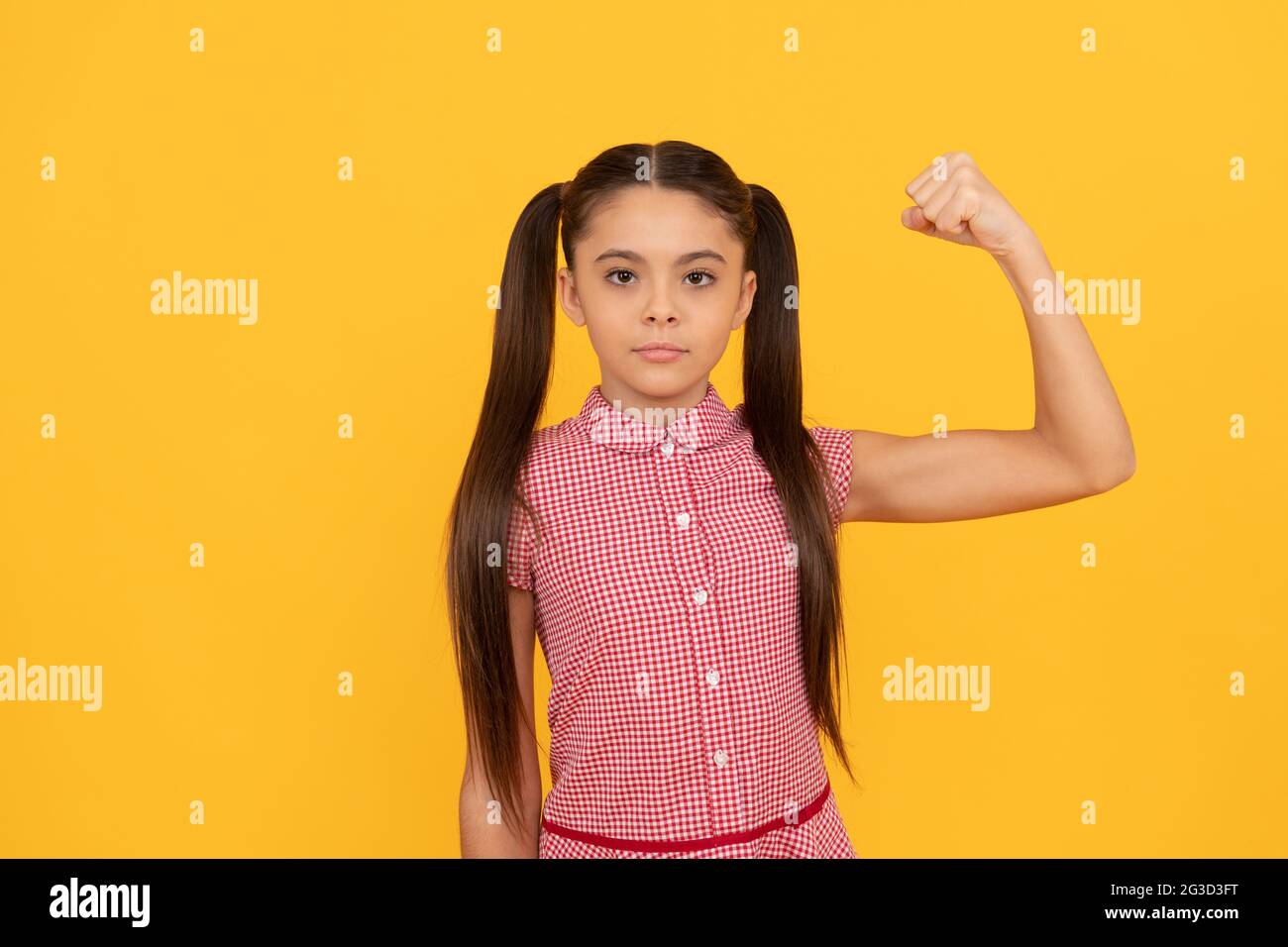 Serious girl child show power gesture flexing arm yellow background, strong Stock Photo