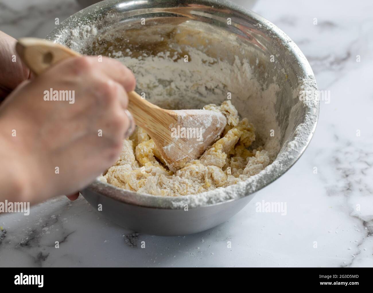 woman hand holding a wooden spoon mixing ingredients in a metal round bowl on a white marble surface Stock Photo