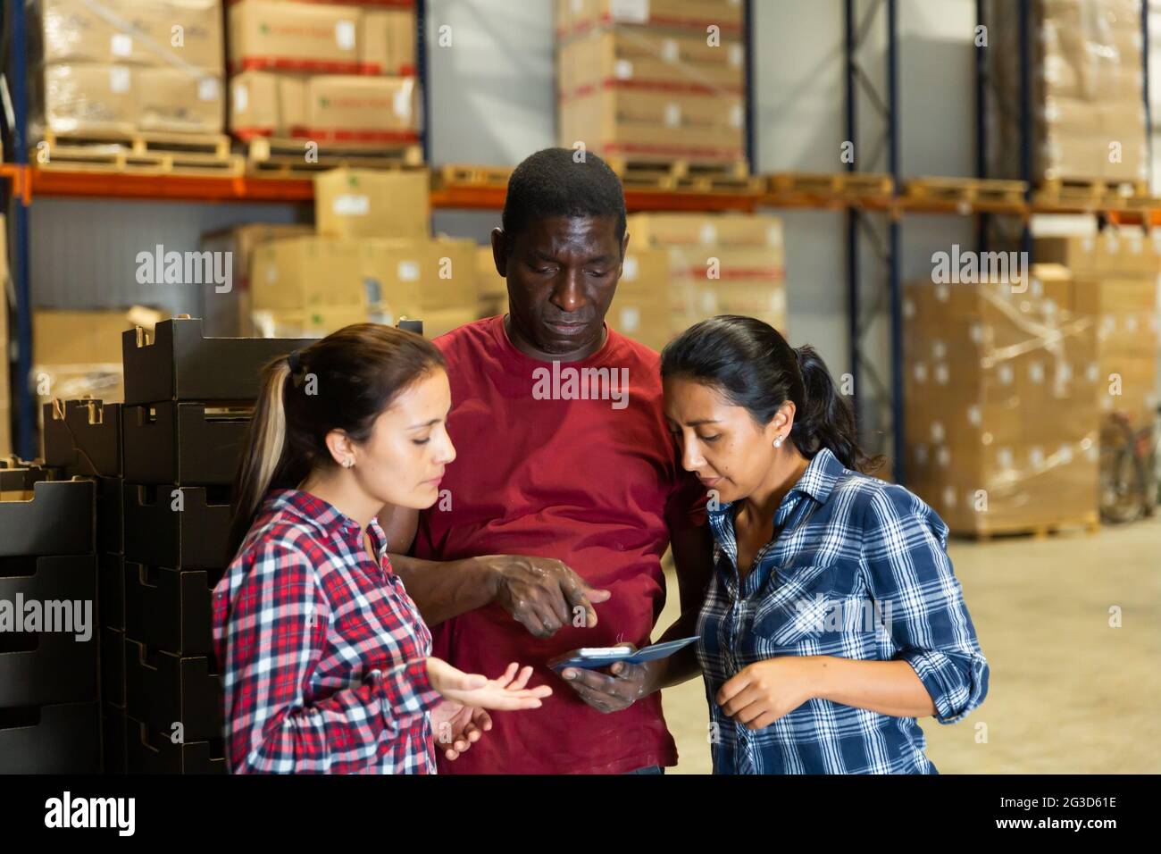 Three workers discussing working process at warehouse Stock Photo