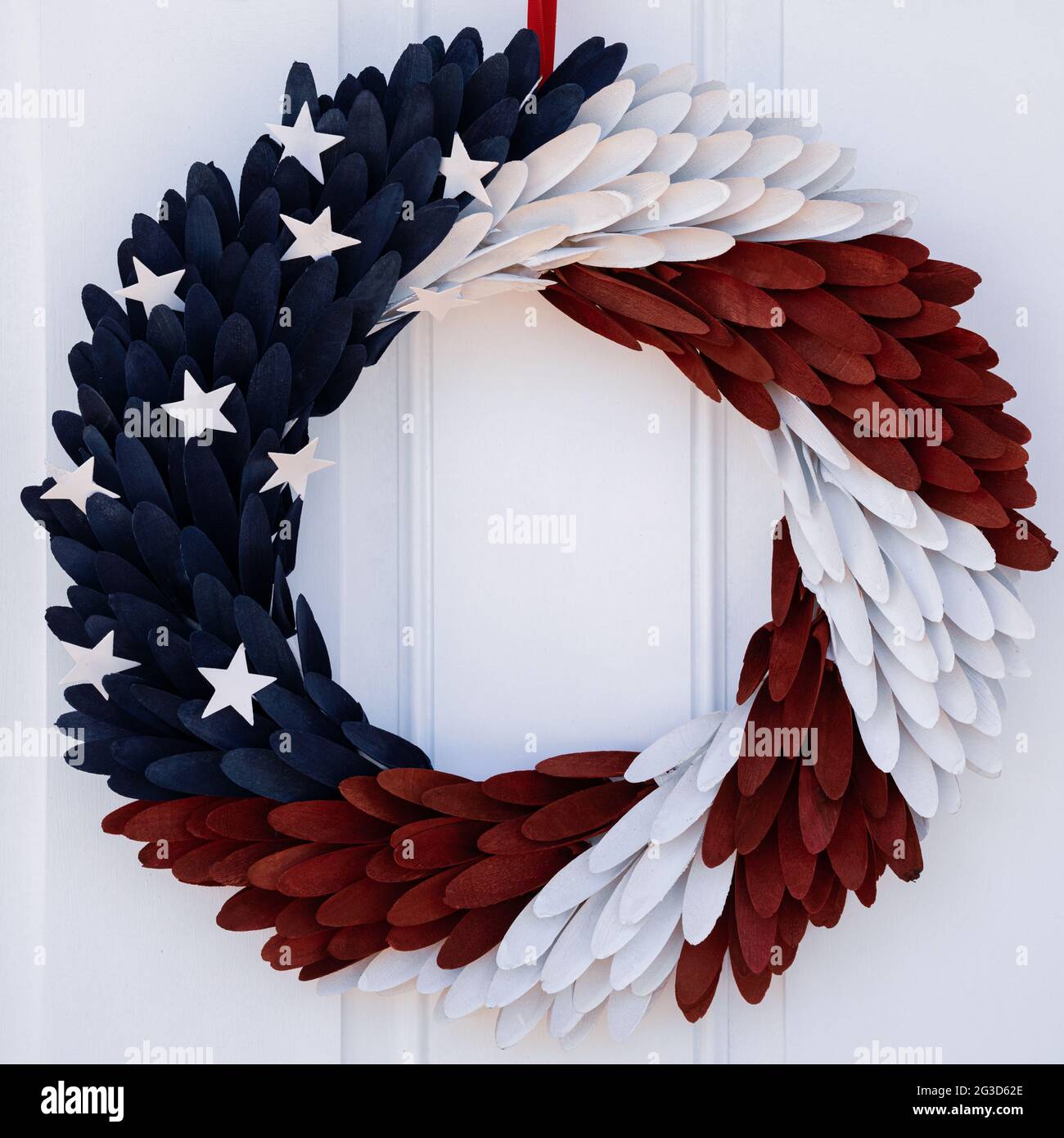 Photograph of a red, white and blue door wreath with stars hung on a white door Stock Photo