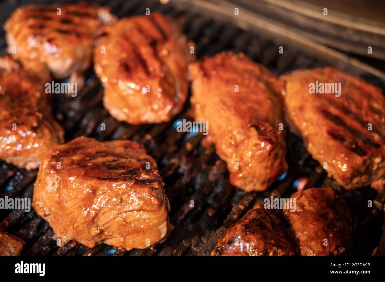 Steaks grilling on a gas barbecue covered in spicy BBQ sauce Stock
