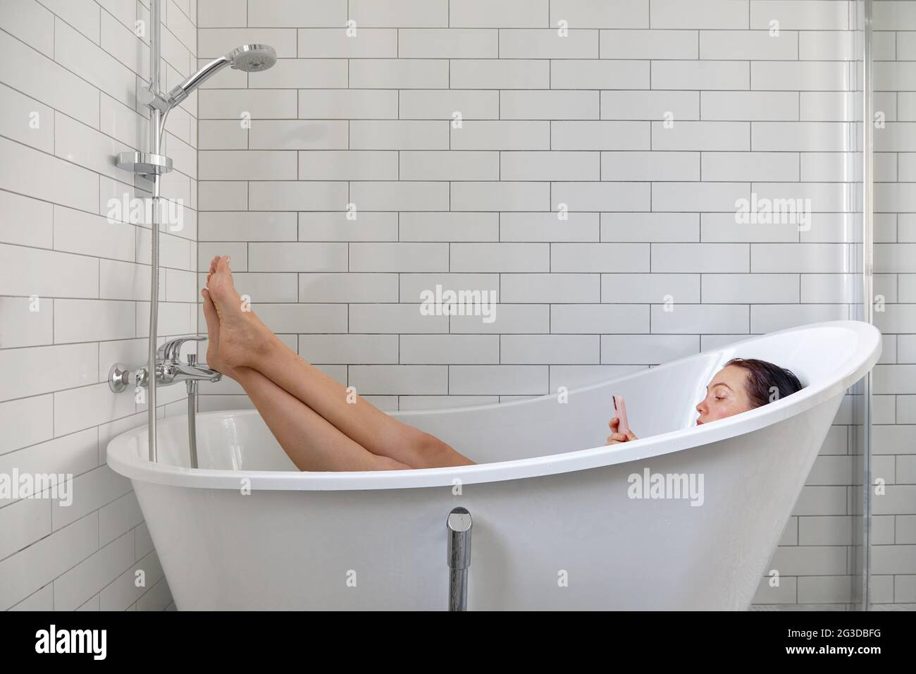 Young female browsing internet on mobile phone while taking bath and relaxing in bathtub Stock Photo