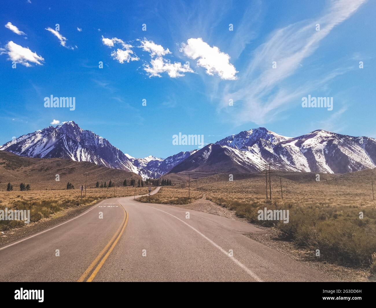 Road to Snow capped Sierra Nevada Mountains blue sky with clouds Stock Photo