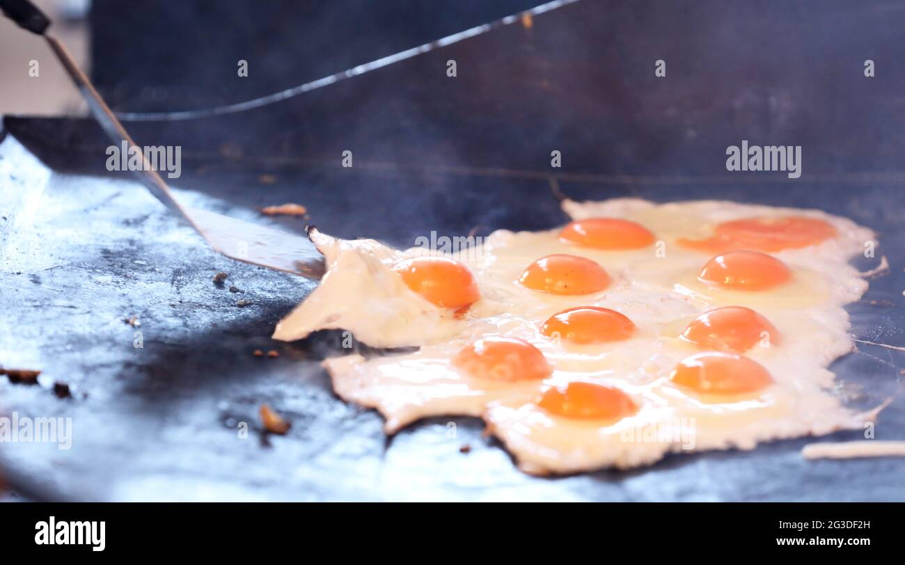 Multiple cracked eggs frying on a bbq grill plate. Egg yolks and whites being fried or cooked in large quantities on a barbecue griller. Community fun Stock Photo