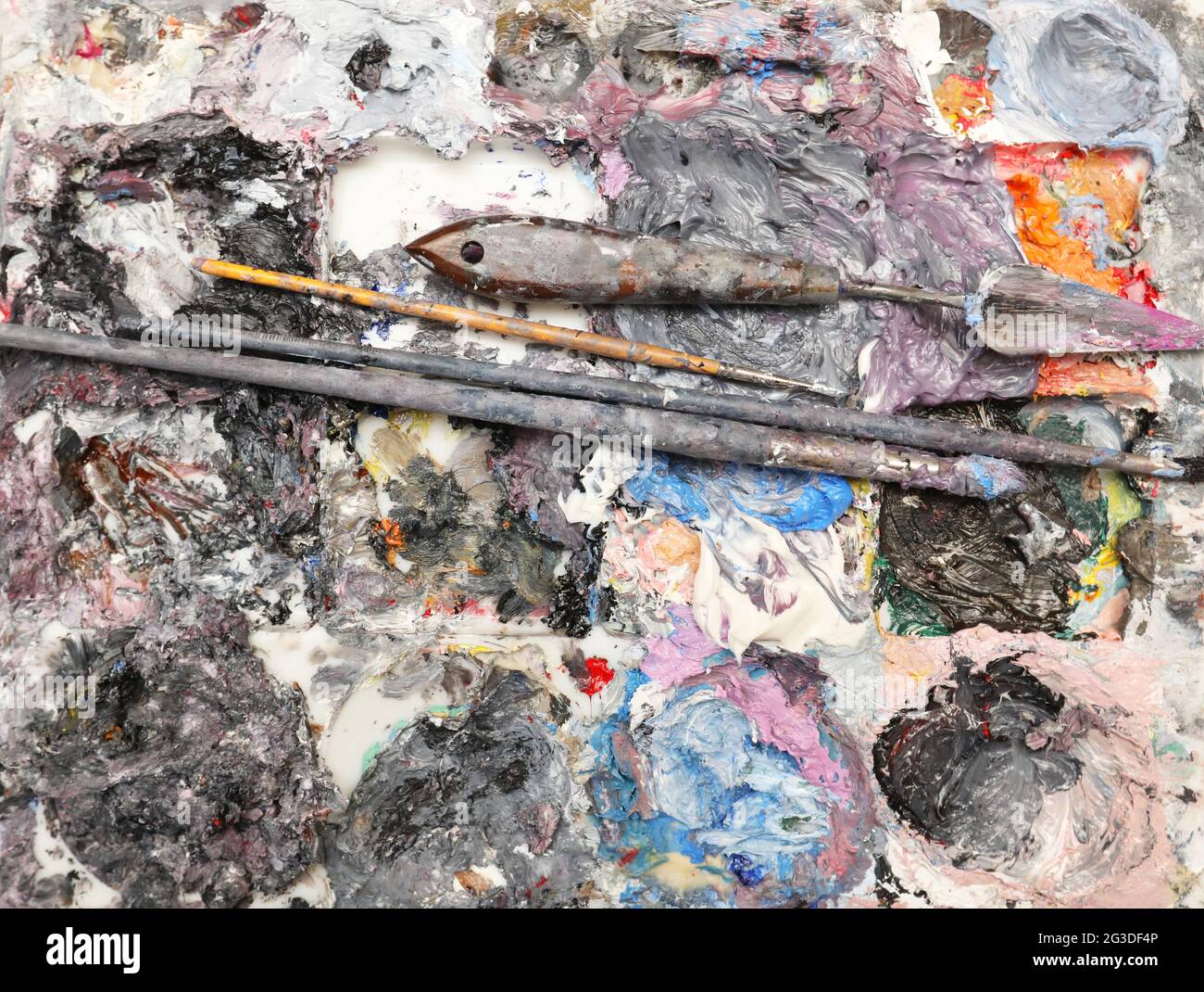 A full view of a artists painting palette loaded with rich thick wet oil paint, brushes and palette modeling knife. Isolated on a white background Stock Photo