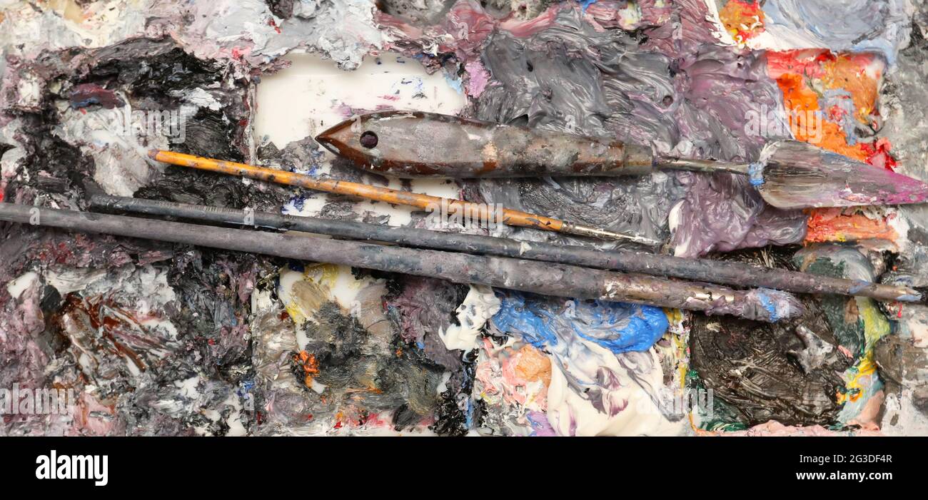 A wide close up view of a artists painting palette loaded with rich thick wet oil paint, brushes and palette modeling knife. Stock Photo