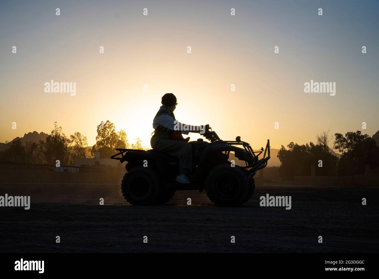 Silhouette of a tourist woman rides a quad bike against the background of a bright sunset. Evening extreme entertainment in the desert of Egypt. Stock Photo