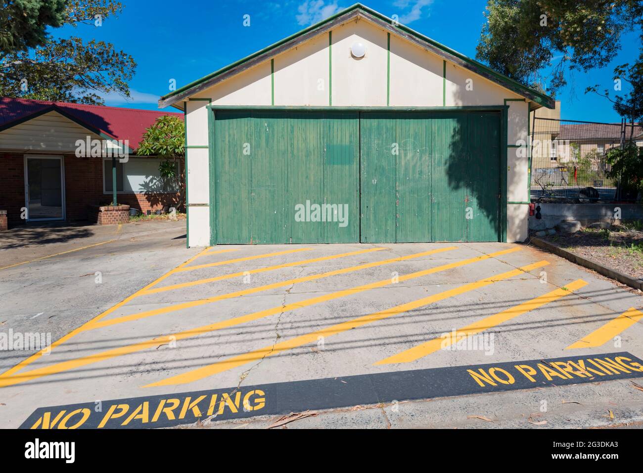 Yellow diagonal painted lines on a concrete driveway mark a no parking zone in front of an old fibro double garage in Sydney, Australia Stock Photo