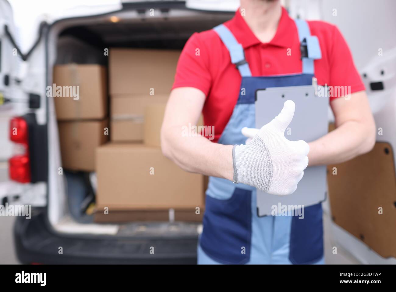 Loader driver in uniform holds a thumbs up in background of car with boxes Stock Photo